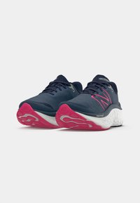 Blauwe hardloopschoenen met een gestructureerde bovenkant, roze accenten op de zool en een witte tussenzool. Kenmerken zijn onder andere veters en een gevoerd ontwerp.