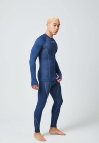 Conjunto deportivo de compresión en azul marino, hecho de material suave y elástico; presenta mangas largas, forma ajustada y patrones de costura clara contrastante.