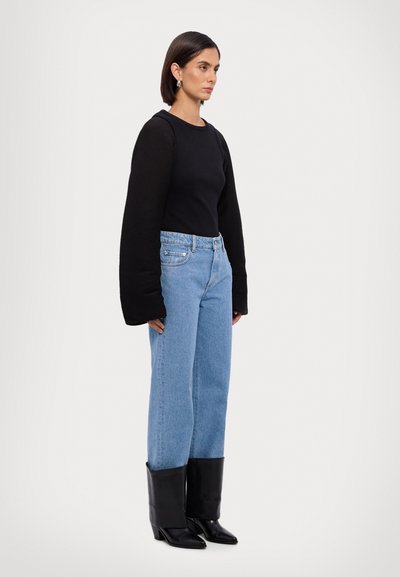 Zwarte lang mouwen top, lichtblauwe highwaisted denim jeans en kniehoge zwarte haklaarzen, wat een gelaagde silhouet creëert.