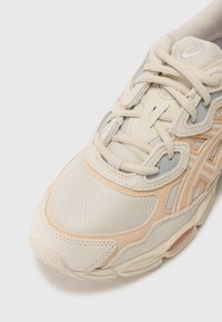 Gai smilškrāsas sporta apavi ar teksturētu mēslu un zamšādas elementiem. Iekļauti maigi persiku toņi un mīksta apkakle; šņorēm ir standarta dizains.