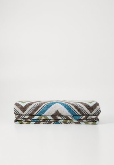 Woven blanket featuring a zigzag pattern in brown, blue, green, and lavender hues. Soft texture, rectangular shape, and folded design.