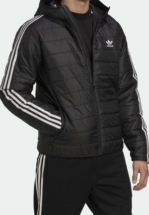 Zwarte gewatteerde jas met capuchon, met witte verticale strepen op de mouwen en een klein wit logo op de borst. Ritssluitingen aan de zakken.