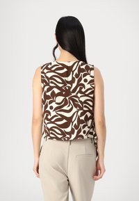 Top senza maniche con motivo marrone e bianco, caratterizzato da una vestibilità rilassata e un orlo arrotondato, abbinato a pantaloni beige. Tessuto di texture liscia.