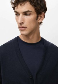 Granatowy kardigan z głębokim dekoltem w serek, wykonany z miękkiego dzianinowego materiału. Posiada pojedyncze zapięcie na guzik i jest noszony na dopasowanej koszulce z okrągłym dekoltem.