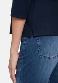 Camiseta azul marino de mangas cortas con aberturas laterales, combinada con jeans de mezclilla de lavado medio que cuentan con un bolsillo trasero con diseño puntiagudo.
