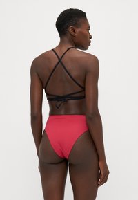 Červené bikiny s vysokým pásom a hladkým povrchom. Čierne krížové popruhy na zadnej strane zodpovedajúceho vršku bikín. Jednoduchý dizajn.
