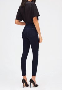 Jeans ajustados de cintura alta en azul oscuro combinados con una camiseta negra de manga corta y tacones altos negros, mostrando un diseño ceñido y detalles mínimos.