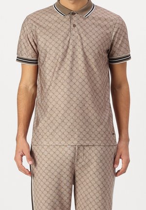 Mand iført beige mønstret poloshirt og matchende bukser med mørkebrunt og hvidt stribet krave og ærmekanter.