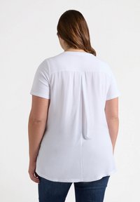 Top bianco a maniche corte con piega sul retro, scollo rotondo e texture liscia. Abbinato a jeans blu.