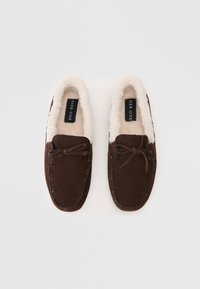Mocasines de ante marrón con forro de lana blanca y un lazo decorativo en la parte superior, etiquetados "Pier One" en su interior.