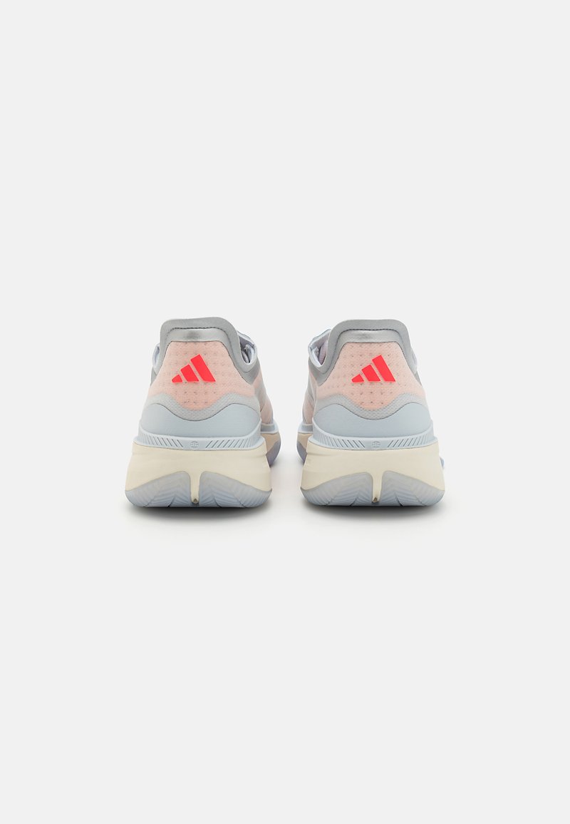 Chaussures de sport gris clair avec des accents roses, dessus en maille texturée, trois rayures rouges au talon et détail élastique autour du col.
