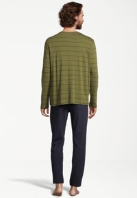 Vihreä oliivi pitkähihainen paita, jossa on ohuita mustia viivoja, yhdistettynä tummansinisiin housuihin. Pehmeä kangas, rento malli ja pyöreä pääntie.