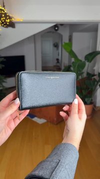 Μαύρο δερμάτινο πορτοφόλι με υφή και φερμουάρ σε χρυσό τόνο. Διαθέτει λογότυπο της μάρκας σε χρυσό μπροστά. Συμπαγής, ορθογώνιος σχεδιασμός.