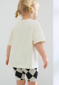 Ljusbeige bomulls t-shirt med korta ärmar, tillsammans med svart- och vitrutiga shorts. Mjuk textur, avslappnad passform.