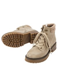 Bottines en daim beige avec semelles épaisses en caoutchouc marron à crampons, lacets sur le devant, fermeture éclair latérale et col rembourré pour plus de confort et de chaleur.