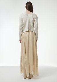 Weißes, plissiertes Oberteil mit langen Ärmeln, kombiniert mit einem leichten, beigefarbenen, fließenden Maxirock. Glatte Textur, minimalistisches Design.