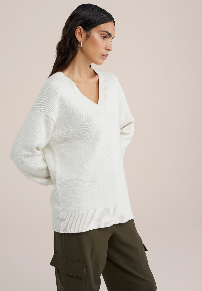 V-Ausschnitt, oversized Pullover aus weichem weißem Strickstoff, mit gerippten Bündchen und Saum, kombiniert mit olivgrünen Cargo-Hosen.