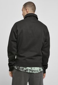 Hanorac negru cu guler înalt, croială supradimensionată și manșete din tricot. Stratul de peste un tricou tie-dye în nuanțe de verde și negru.