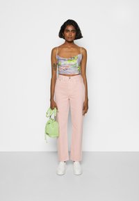 Top cropped floral lilás claro com alças finas, combinado com calças de perna larga rosa pastel de cintura alta e uma pequena mala verde. Ténis brancos.