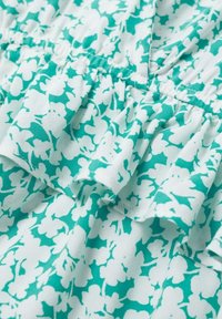 Tejido con patrón floral en tonos turquesa y blanco, con un detalle de volantes texturizado. El material parece ligero y suave.