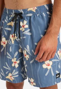 Modré kvetinové plavky s pásom na stiahnutie. Obsahujú biele a žlté kvety hibiscus, čierne akcenty a ľahký materiál.