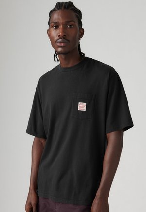 Black cotton t-shirt with a crew neck and short sleeves, featuring a small left chest pocket with a red label. Smooth texture and relaxed fit.