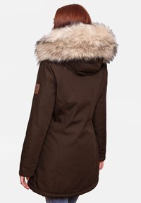 Bruine parka met een met bont afgewerkte capuchon, voorzien van een patch op de mouw en een gebogen zoom. Zachte textuur en gestructureerd ontwerp.