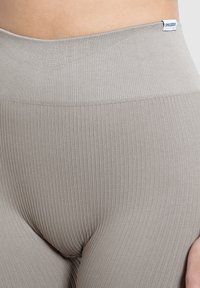 Beige geribbelde leggings met een hoge, elastische tailleband. Heeft een zachte textuur en een klein merklabel aan de bovenkant.