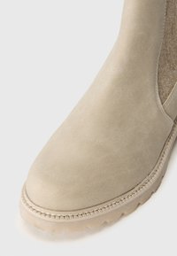 Beige mocka ankelstøvler med en rund tå, teksturert innside og robust gummisåle. Har synlig søm langs kanten.