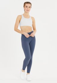 Ljusgrå sport-bh i kombination med högmidjade, marinblå leggings. Leggingsen har en slät textur och minimala sömnadsdetaljer.