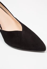 Chaussure plate en daim noir à bout pointu avec une doublure intérieure beige sur fond blanc.