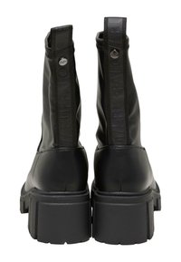 Botas de cuero negras hasta el tobillo con una suela gruesa, que presentan un tirador trasero texturizado y una marca en relieve a lo largo del lado.