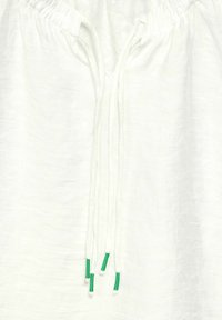 Haut en lin blanc avec un décolleté froncé et des cordons réglables, accentués de pointes vertes. Texture lisse et design léger et aéré.