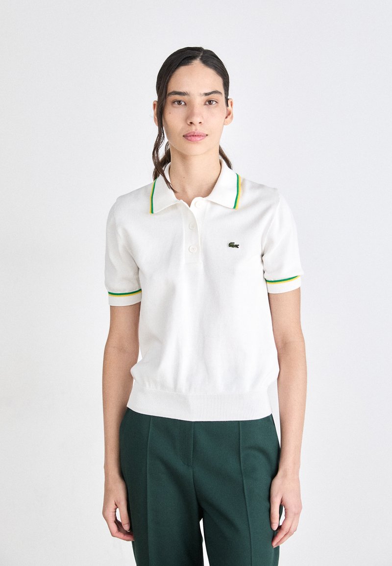 Witte polo-shirt met groene en gele gestreepte kraag en mouwcuppen, voorzien van een klein geborduurd logo op de borst en een geribde zoom.
