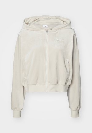 Skórzana beżowa bluza z kapturem wykonana z miękkiej tkaniny, z zapięciem na zamek błyskawiczny, bocznymi kieszeniami oraz logo na górnej lewej stronie klatki piersiowej.