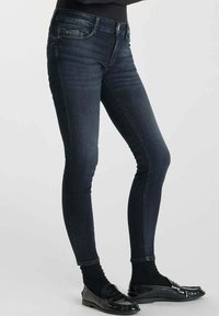 Jeans ajustados de color azul oscuro con una textura vaquera suave, que presentan un cierre frontal de botón y cremallera, cinco bolsillos y un silueta entallada.