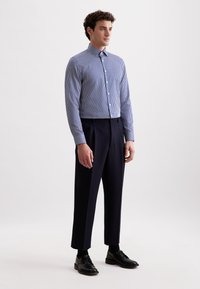 Camicia a righe blu e bianche con colletto a bavero, abbinata a pantaloni plissettati blu scuro e scarpe con lacci nere.