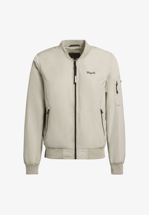 Giacca bomber beige chiara con zip frontale, polsini a costine, tasche laterali e tasca sulla manica. Texture liscia con branding minimo.