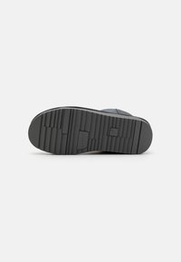 Suola di scarpa in gomma nera con texture, caratterizzata da scanalature orizzontali e verticali per una migliore aderenza; include un piccolo logo vicino al tallone.