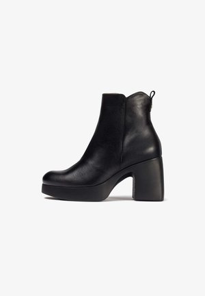 Botín de cuero negro hasta el tobillo con punta redonda, tacón alto grueso y suela texturizada. Presenta una cremallera y una cinta en la parte trasera.