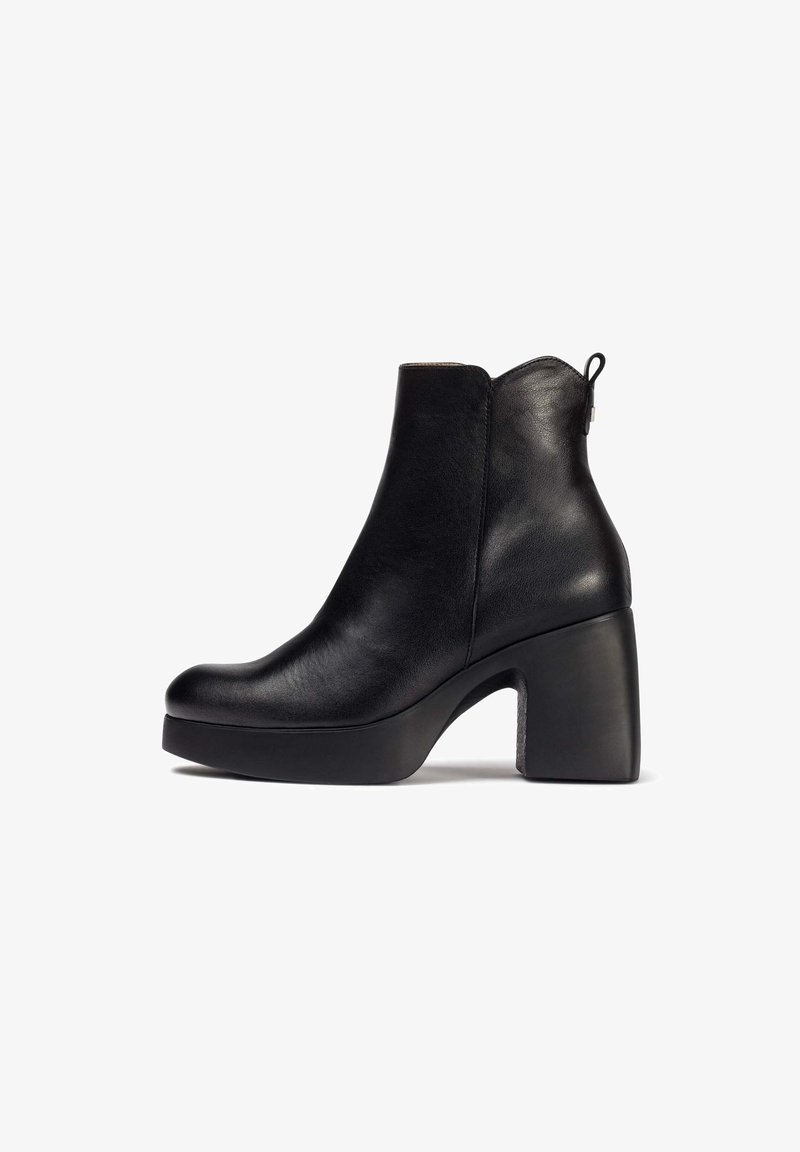 Zwarte leren enkelboot met een ronde neus, stevige hoge hak en getextureerde zool. Beschikt over een ritssluiting en een trekband aan de achterkant.