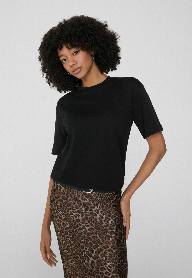 Czarny top z krótkim rękawem i okrągłym dekoltem, zestawiony z spódnicą w lamparcie cętki o gładkiej fakturze i czarnym paskiem jako akcentem.