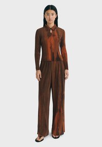Bruine gestreepte gebreide twee-delige outfit met een kraag, lange mouwen en een sleutelgatdetail bij de hals. Loszittende broek maakt de set compleet.