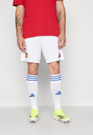 Shorts de football blancs avec un logo rouge, associés à un maillot rouge. Comprend des chaussettes rayées bleues et des chaussures de sport jaune vif avec des accents noirs.