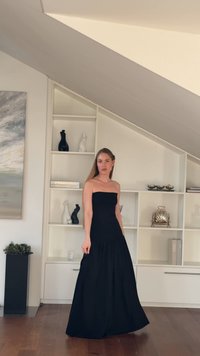 Black strapless maxi dress with a fitted bodice and flared tiered skirt. Smooth fabric, minimalistic design, and floor-length silhouette.