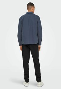 Camicia navy a maniche lunghe, vestibilità morbida, abbinata a pantaloni neri. La camicia presenta un colletto classico e una texture di tessuto liscia.