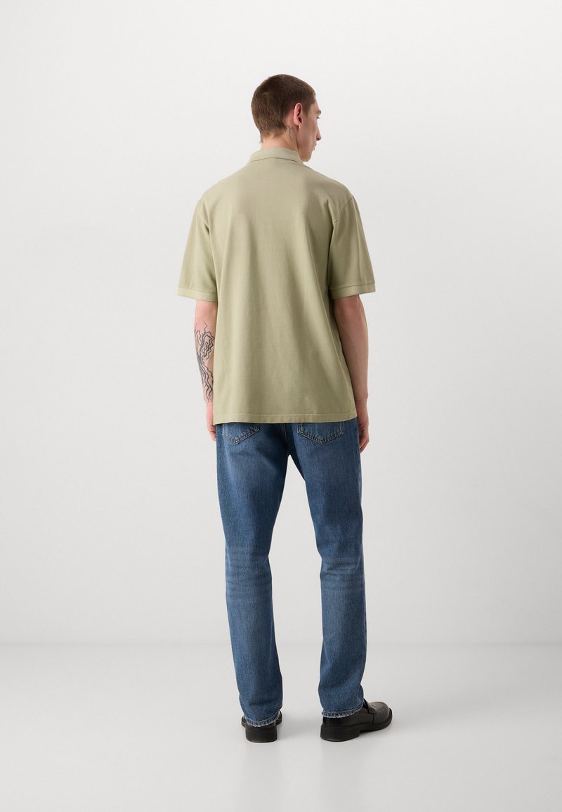 Polo shirt pour homme vert clair à manches courtes, coupe décontractée, associé à un jean en denim bleu et des chaussures noires, vu de dos.