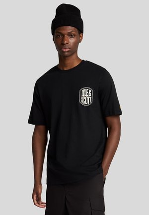 Sort bomulds t-shirt med korte ærmer, der har et hvidt og guld logo patch på venstre bryst. Kombineret med sorte cargo shorts og en strikket hue.