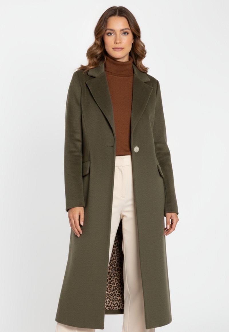 Olivengroene wollen jas met een geremde reverskraag, enkele knoopsluiting en leopardprint voering; gedragen over een bruine coltrui en crèmekleurige broek.