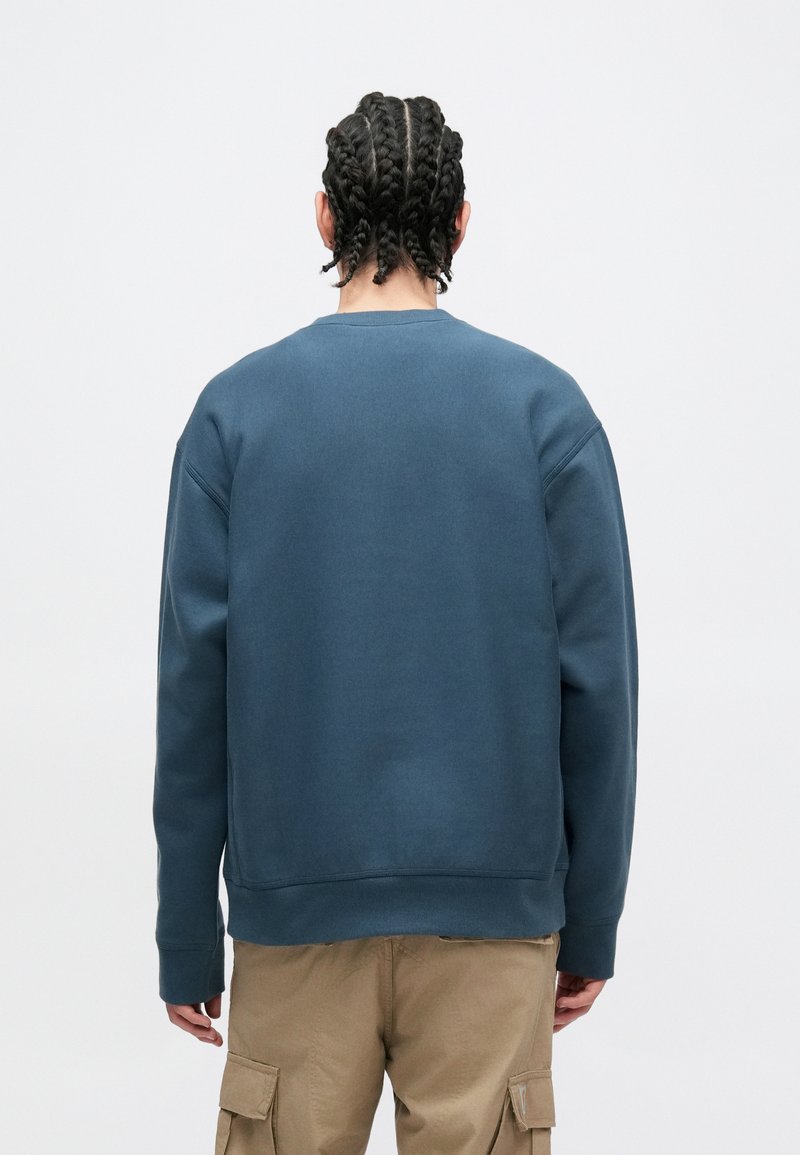 Mørkeblå sweatshirt med rund hals, ribstrikkede manchetter og kant; glat tekstur; båret med beige cargobukser.